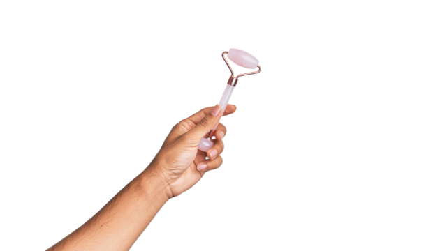Hand holding a pink facial roller with a metal frame and a cylindrical stone at the end, arm extended. clean white background