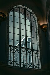 Architectural view of an ornate arched window with wrought iron details reflecting a tall building in an urban setting