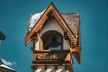 Close-up of a rustic wooden bell tower with snow on the roof under a clear blue sky showcasing traditional alpine architecture