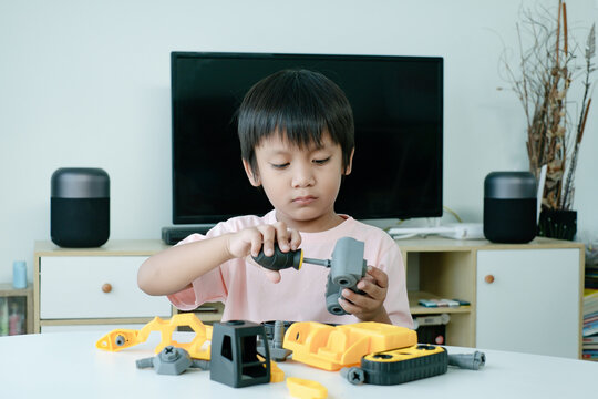 Adorable Asian boy using screwdriver toy. Kid assembly technician skills development.