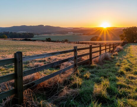 Sunrise over a rural landscape with a wooden fence and frosty fields.
