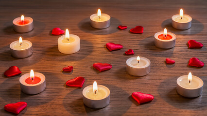 Romantic composition: burning tealight candles and red hearts on a wooden background.