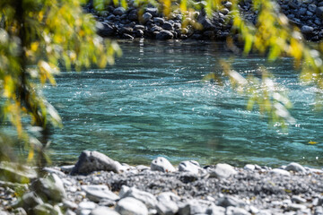 Fototapeta premium Turquoise river flowing between rocks on a sunny autumn day, surrounded by warm fall colors and clear water, showcasing a serene alpine landscape