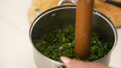 Chef crushing fresh green onions in stainless steel pot