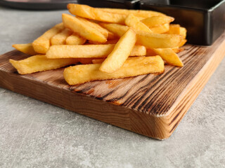 Golden crispy French fries on old wooden board on table in cafe. Potatoes lightly sprinkled with salt. Close-up.