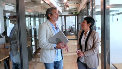 Professional business colleagues discussing a project while walking in a modern office corridor - Powered by Adobe