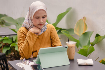 An young Asian Muslim businesswoman working remotely in an outdoor cafe using a tablet
