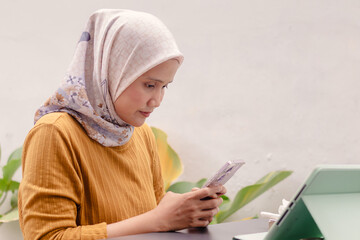 An Asian Muslim businesswoman replying a message on her smartphone at an outdoor cafe