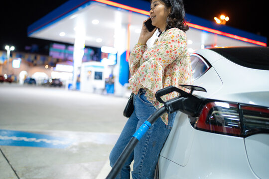 Business asian tourist woman use smartphone waiting ev car charge station at night