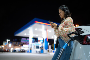 Business asian tourist woman use smartphone waiting ev car charge station at night