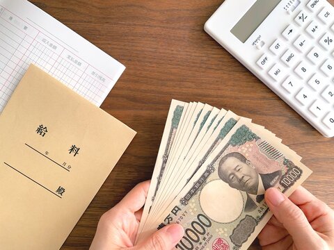 机上で紙幣を持つ女性の手と給料袋／給料日イメージ