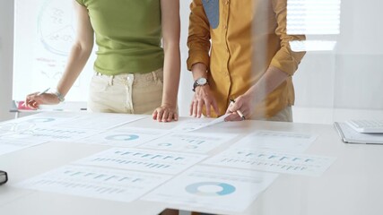 Professional team collaborating, reviewing financial documents and graphs on laptop with printed data spread across conference table in contemporary workspace. Business people concept