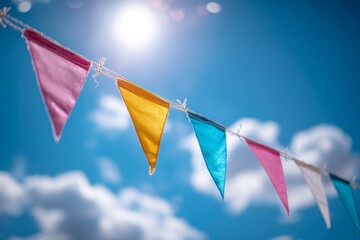 Vibrant colorful pennant flags hanging on a string against a bright blue sky with fluffy clouds and shining sunlight during a festive outdoor celebration