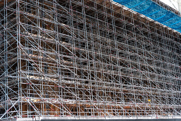 Scaffolding surrounds a seven‑story building in England, providing essential safety for construction workers and protecting the public below with a blue safety net