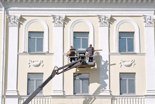 Elevated maintenance crew using mechanical lift to access the third floor of classical building, facade restoration and exterior cleaning operations. Workers in lift bucket paint building wall