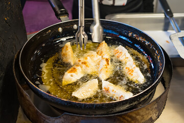 Close-up of dumplings being deep-fried in a pan with hot oil using metal tongs at a street food or market stall