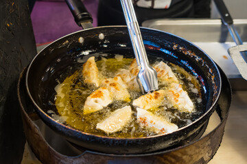 Close-up of dumplings being deep-fried in a pan with hot oil using metal tongs at a street food or market stall