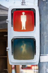 Close-up of a pedestrian traffic light showing a red stop signal with a stylized male figure wearing a hat
