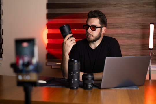A man is recording a video blog about camera equipment at his desk