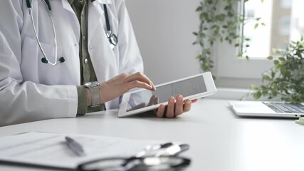 Female doctor in lab coat and stethoscope using digital tablet at desk in medical office, accessing online patient information. Medicine and health care concept - Powered by Adobe