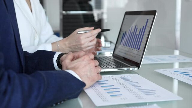 Business professionals examining laptop charts and bar graphs during a modern office meeting, discussing sales performance, market trends, financial analysis and strategy development