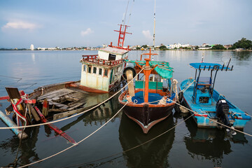 Traditional wooden fishing boats docked in a calm harbor with ropes and nets visible during a peaceful seaside day