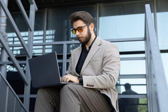 A man is sitting on the stairs while looking at his phone and holding a tablet