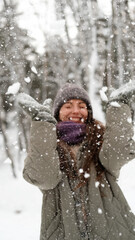 Fototapeta premium A beautiful young woman in winter clothes is happily spending her free time in a snowy forest. She enjoys the first snow. Active winter recreation.
