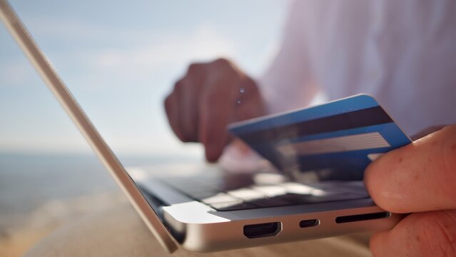 A digital nomad works on a laptop at a remote location, holding a credit card. The scene highlights freelance work, emphasizing freedom and portability, blending technology and travel seamlessly. - Powered by Adobe