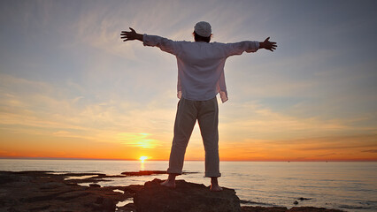 A silhouette stands on a rocky shore at sunset, arms outstretched, embodying mindfulness and...
