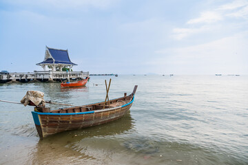 Traditional red fishing boat floating on calm sea with several other boats in the distance on a cloudy day