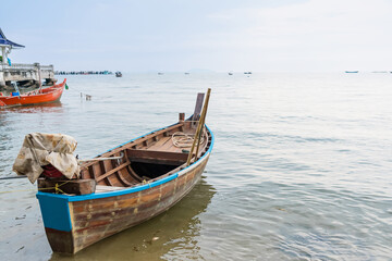 Fototapeta premium Traditional red fishing boat floating on calm sea with several other boats in the distance on a cloudy day