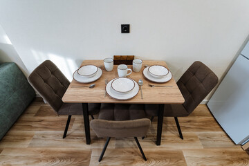 rustic wooden dining table set four with neutral ceramic plates and mugs, upholstered chairs, natural light, textured tabletop and relaxed cozy atmosphere for casual breakfast or dinner