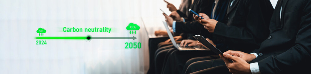 Business professionals engage in a discussion about carbon neutrality timelines, focusing on sustainability goals from 2024 to 2050 while using modern technology. Trope