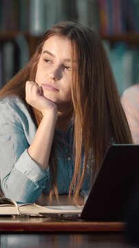 A woman student ponders thoughtfully while studying in a library setting today