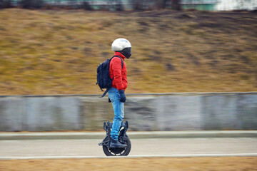 Person riding an electric unicycle wearing helmet and backpack along an urban road in motion. Commuter with protective helmet and backpack balancing on electric unicycle. Motion blur. Selective focus © Tricky Shark