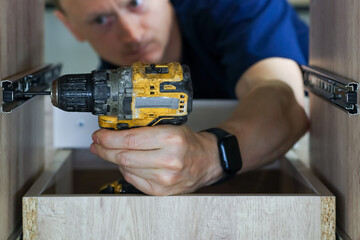 Craftsman using drill to secure drawer runner in cabinet