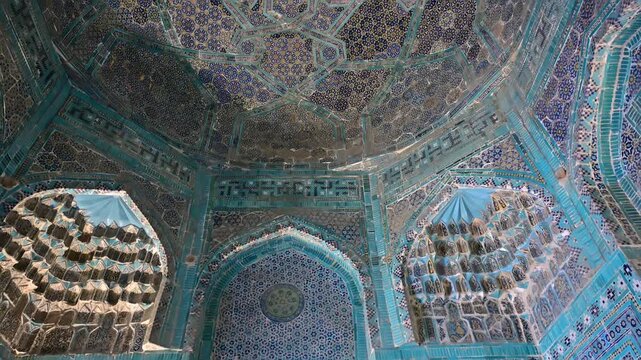 Vertical pan showing the ornate blue-tiled mausoleums of Shah i Zinda in Samarkand, Uzbekistan, under bright daylight.