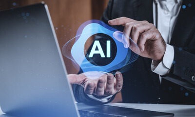 Businessman interacting with glowing AI hologram above laptop in modern tech office environment, symbolizing artificial intelligence innovation concept.