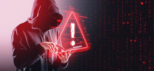 Hacker in hoodie using tablet with digital warning sign and bina
