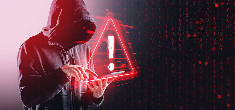 Hacker in hoodie using tablet with digital warning sign and bina