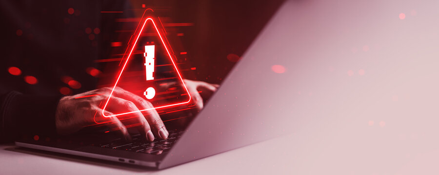 Cybersecurity warning alert on laptop screen with hands typing in dark red environment, digital glitch effects and creative concept background.