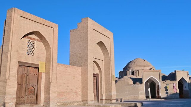 A view of the Toqi Telpak Furushon bazaar passage in Bukhara, Uzbekistan, featuring domed brick architecture and a passing bicycle on the historic street.