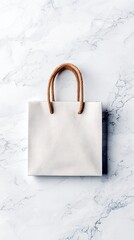 A plain white paper shopping bag with twisted brown rope handles sits centered on a bright white marble surface.