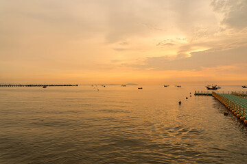 Tranquil seascape at sunset with calm waters, distant fishing boats, and a floating dock extending into the sea