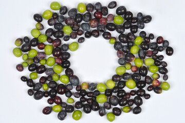 An overhead shot of a wreath or ring created from assorted fresh green and black olives on a clean white background with a center copy space