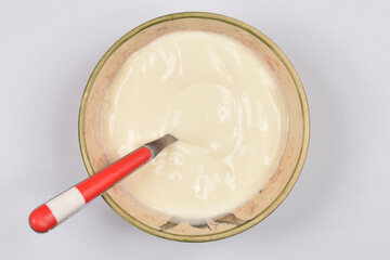 A top-down studio shot shows a creamy white chocolate pudding or custard in a rustic gold-rimmed bowl with a metal spoon resting inside, all on a white background.