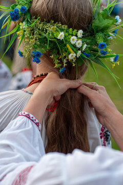 Close up rear view of hands braiding long hair of a girl wearing a traditional Ukrainian floral wreath and embroidered shirt vyshyvanka during traditional Ivana Kupala holiday celebration event
