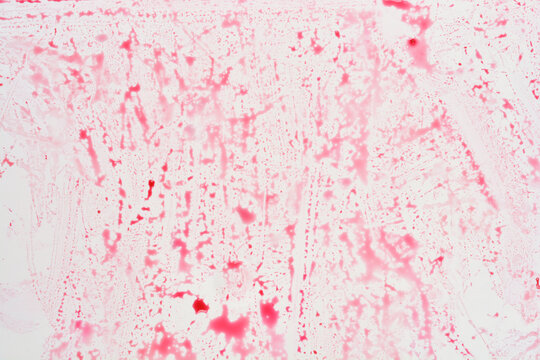 A light surface is covered with an abstract texture of faded and streaked red liquid or food coloring, creating a messy pattern
