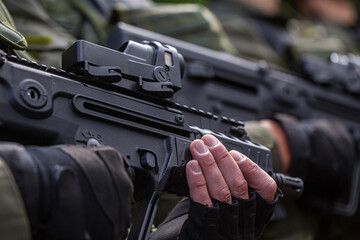 Close up side view of a row of soldiers in green gear holding modern black bullpup assault rifles with red dot collimator sights ready for dangerous military combat defense war operation